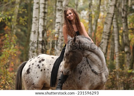 Young girl with appaloosa horse in autumn forest