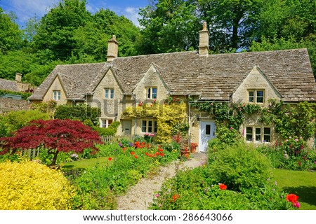 A beautiful row of Cotswold country Cottages and gardens in summer with blue sky and clouds, in the heart of The Cotswolds, Gloucestershire, United Kingdom