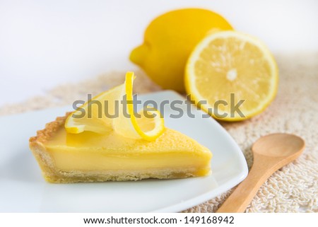 a piece of lemon tart on a white plate decorated with lemons and wooden spoon