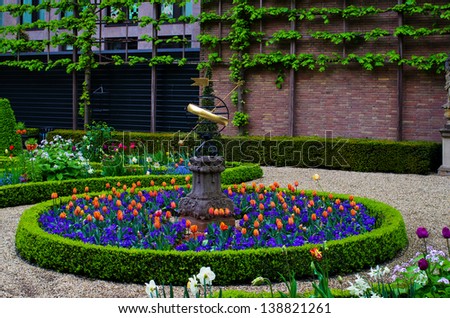 The garden of the Amsterdam canal house Willet Holthuysen with sundial and mixed flower border of orange tulips and blue violets.