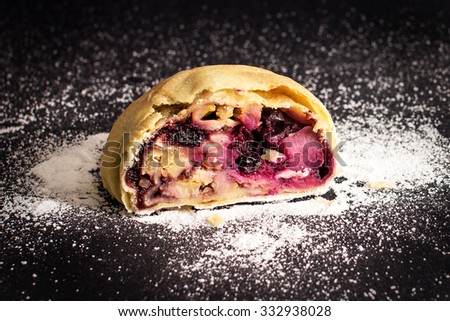 Slice of fresh baked homemade apple strudel with berries and sugar powder, isolated on a black background