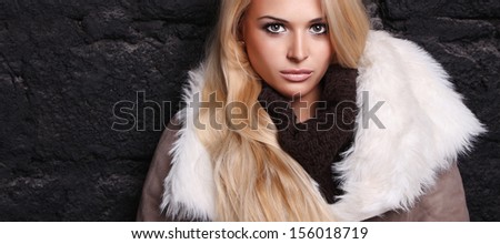 Beautiful blond woman in a fur near bricks wall. winter fashion. your text here. long hair