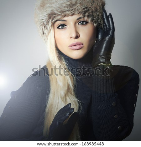 Beauty Fashion blond Girl in Fur Hat. Beautiful Blond Woman in Leather Gloves. Black sweater. Winter Fashion. Gray Background