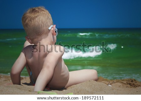 Little boy on the beach. child sitting in sand. looking at sea. Summer. Green sea. Blue sky