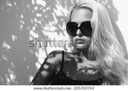 fashion monochrome portrait of beautiful woman in sunglasses.shadows on the face.blond girl near the wall