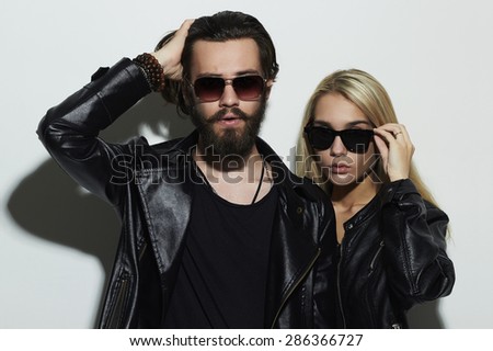 Portrait of gorgeous fashion beautiful couple in black clothes wearing trendy glasses and posing over white background together. Hipster boy and girl. Bearded young man and blonde in sunglasses
