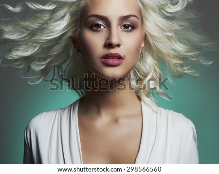 Fashion portrait of young beautiful woman. Flying hair Blond girl. Curly hairstyle.green background