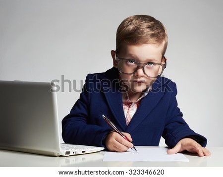 Young businessman using a laptop. funny child in glasses. Fashion portrait of little handsome boy in office