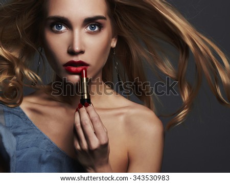 fashion portrait.beautiful girl with red lips. young Woman putting red lipstick. flying blond hair