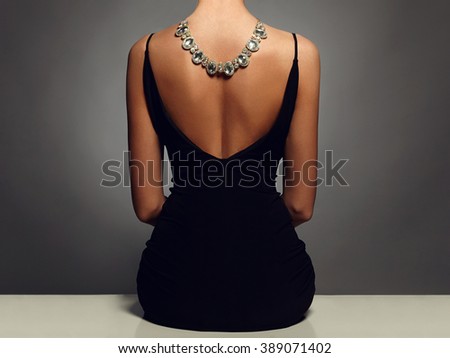 beautiful back of young woman in a black sexy dress.luxury.beauty sitting girl Girl with a necklace on her back.Elegant fashion glamor photo