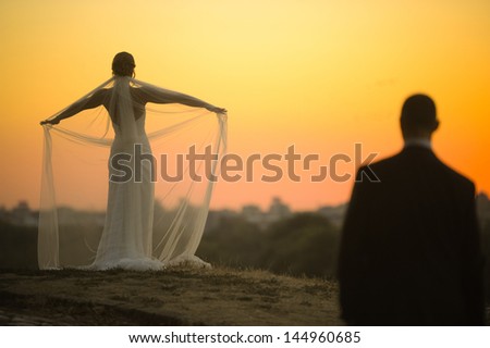 The groom looking at the bride in her wedding dress on sunset