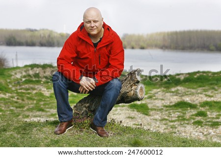 A man in a red jacket sitting on the tree in nature