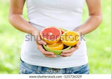 Young woman holding bowl filled oranges and grapefruits
