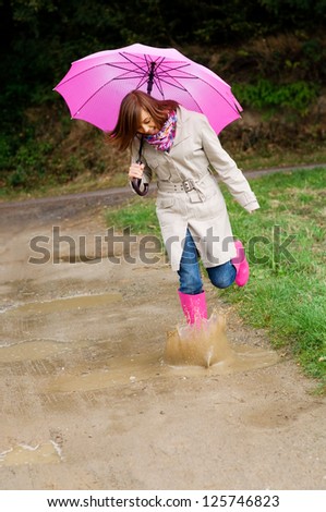 Young woman with rubber boots jumping in puddle