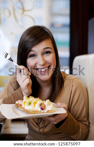 Young woman eating waffles with whipped cream and fruits