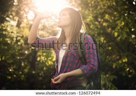 Beautiful female hiker drinking water in forest at sunset