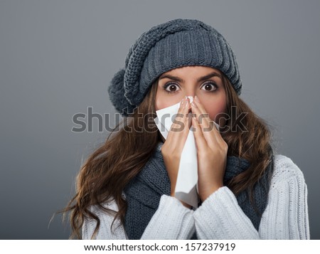 Young woman wearing warm hat sneezing
