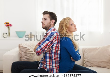 Angry young couple sitting back to back at home