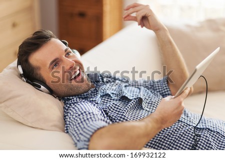 Happy man listening music and lying down on sofa