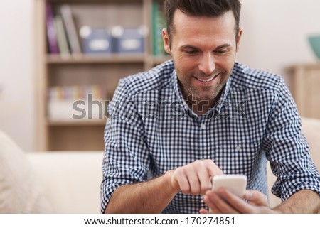 Happy man using mobile phone at home in living room
