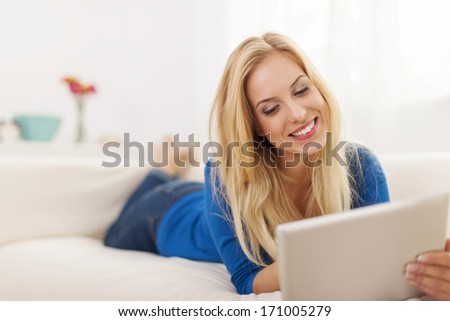Beautiful woman lying down on couch and using digital tablet