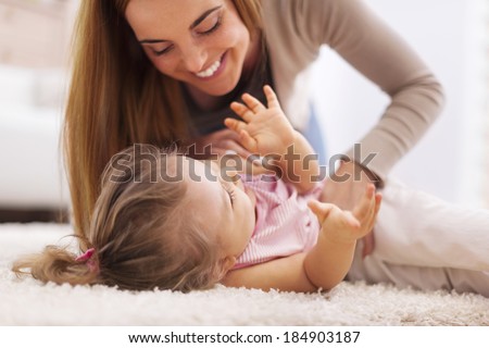 Loving mother playing with little girl on carpet