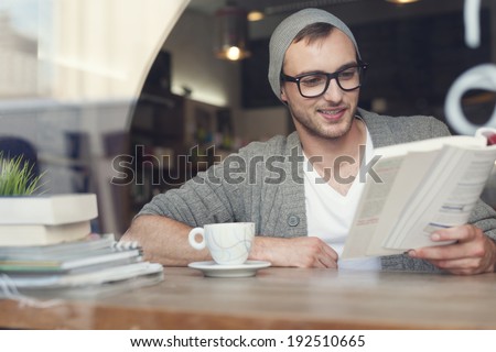 Smiling hipster man reading book at cafe