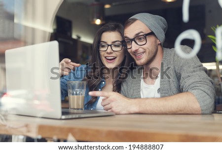 Couple have fun while looking on laptop at cafe