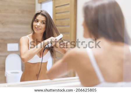 Smiling woman straightening hair in front of mirror