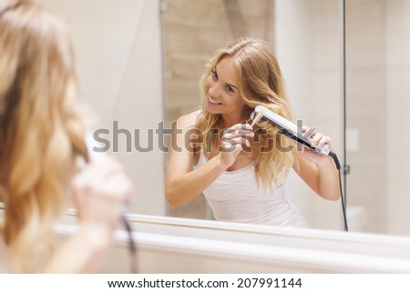 Young women curling hair by straightener