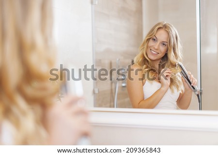 Blonde women curling hair by straightener