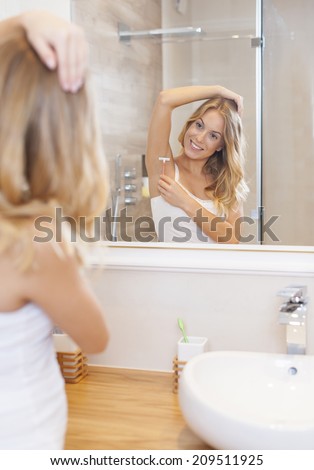 Blonde woman shaving armpit in front of mirror