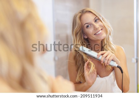 Lovely blonde women curling hair by straightener