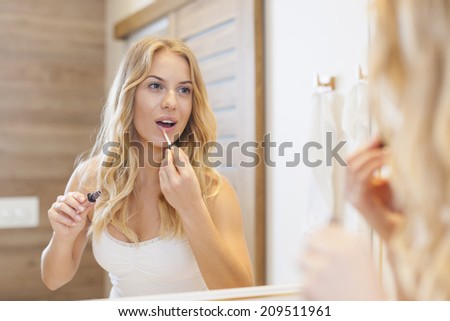Blonde woman finishing makeup in front of mirror