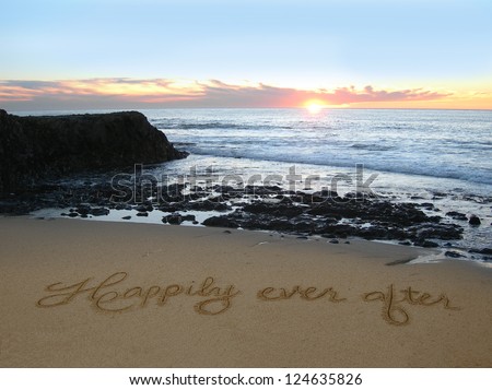 Happily Ever After handwritten in sand with rocks jutting out in background