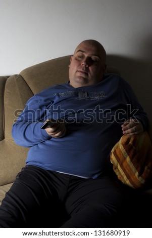 Fat obese man on the couch with remote in one hand