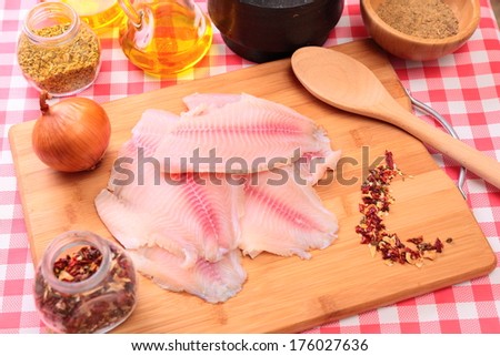 Raw fish tlapia on cutting board surrounded by spices, herbs and seasonings, selective focus
