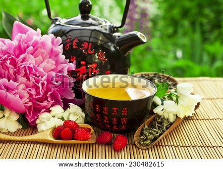 Teapot with bowl of jasmine green tea and peony flower
