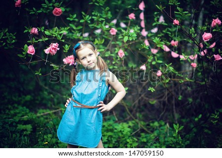girl stands in the bush with pink flowers, smiles