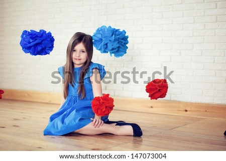 girl in a blue dress sitting on the floor, hanging around the voluminous red and blue flowers, smiles