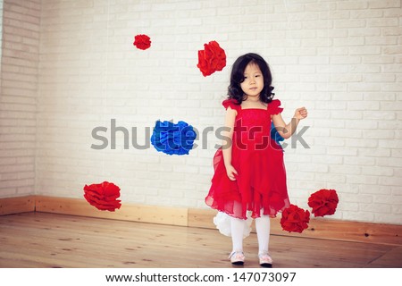 girl in a red dress stands, hanging around the voluminous red and blue flowers, smiles