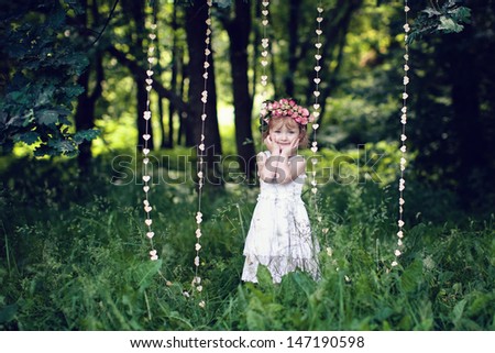 girl standing in the park, on a head a wreath of flowers, in his hands holding a bouquet of flowers. smiles