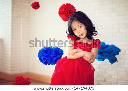 girl in a red dress is standing in a room, hung around a bulky red and blue  flowers from paper, smiles