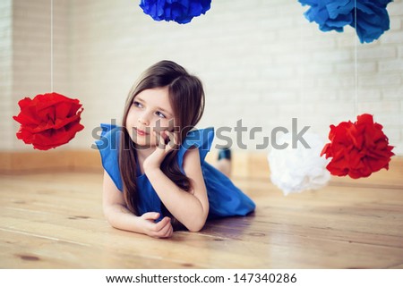 brunette girl in blue dress lying on the floor, hanging around her voluminous blue, red and white flowers made ??of paper.her hand near face