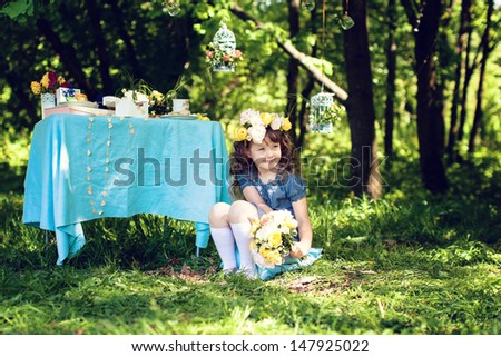 girl sitting outdoors, on the head a wreath of flowers, bouquet of flowers lying near. near it is a table