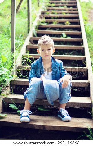 boy sitting on the steps, holding hat, dressed in a blue suit