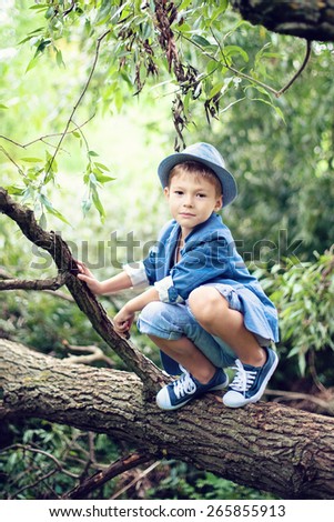 Boy sitting on a tree branch, dressed in a blue suit and hat