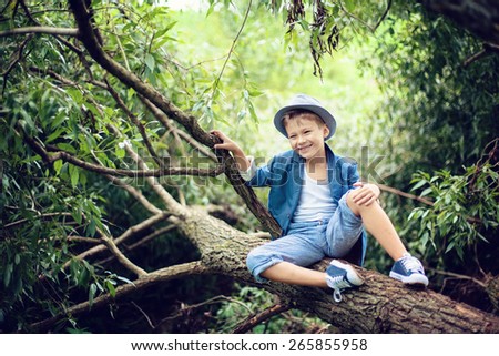Boy sitting on a tree branch, dressed in a blue suit and hat, laughs