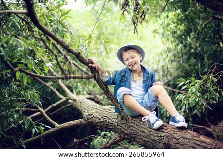 Boy sitting on a tree branch, dressed in a blue suit and hat, laughs