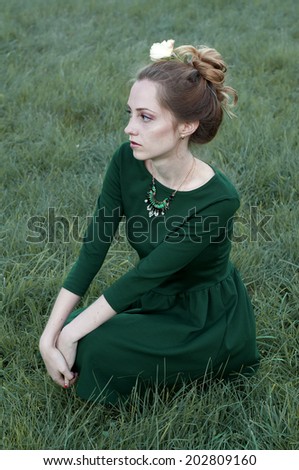 Cheerful caucasian woman with green eyes and green dress sitting outdoors and  looking away